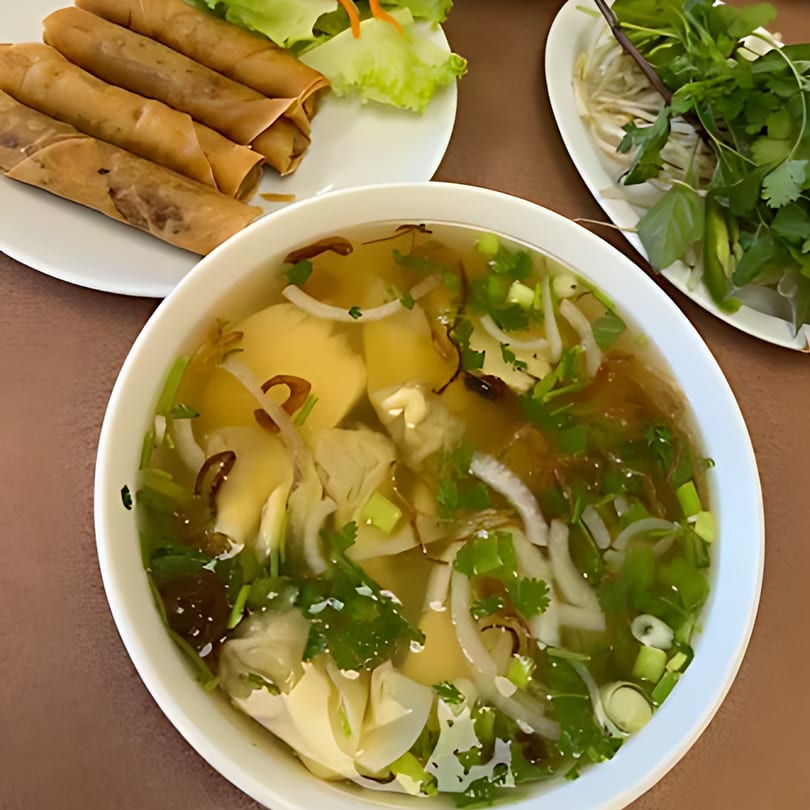 A bowl of Pho Teresa's Vietnamese pho with spring rolls and fresh herbs on the side.