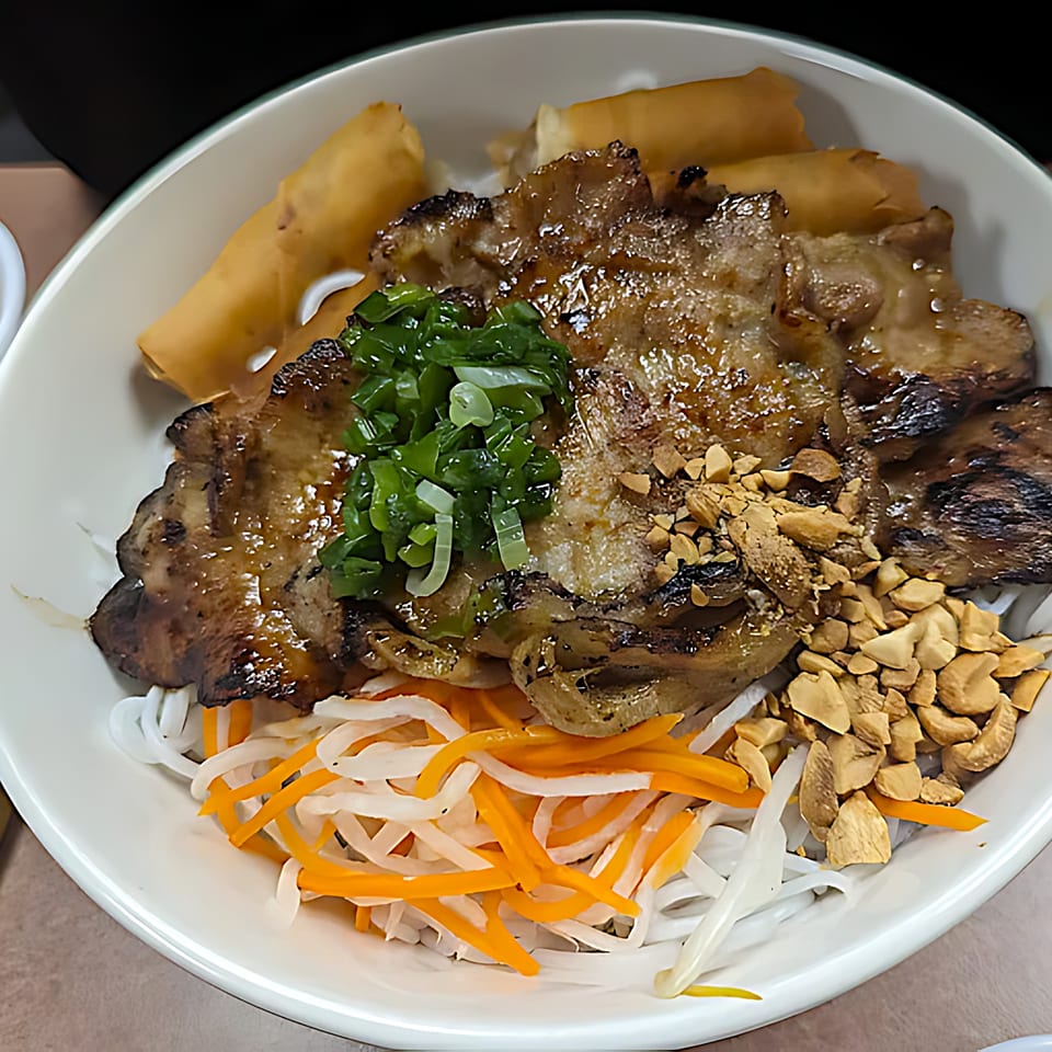 Vietnamese grilled pork and egg rolls over vermicelli noodles, topped with peanuts, scallions, and pickled vegetables.