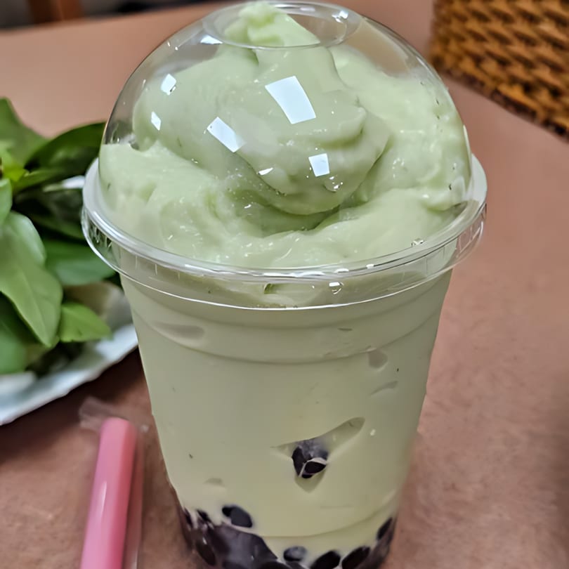 A green avocado bubble tea with tapioca pearls and a domed lid, next to a pink straw.