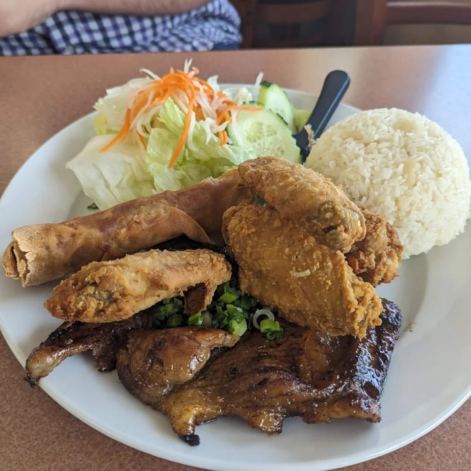 A Vietnamese combo plate with fried chicken, grilled pork, egg roll, rice, and a side salad.