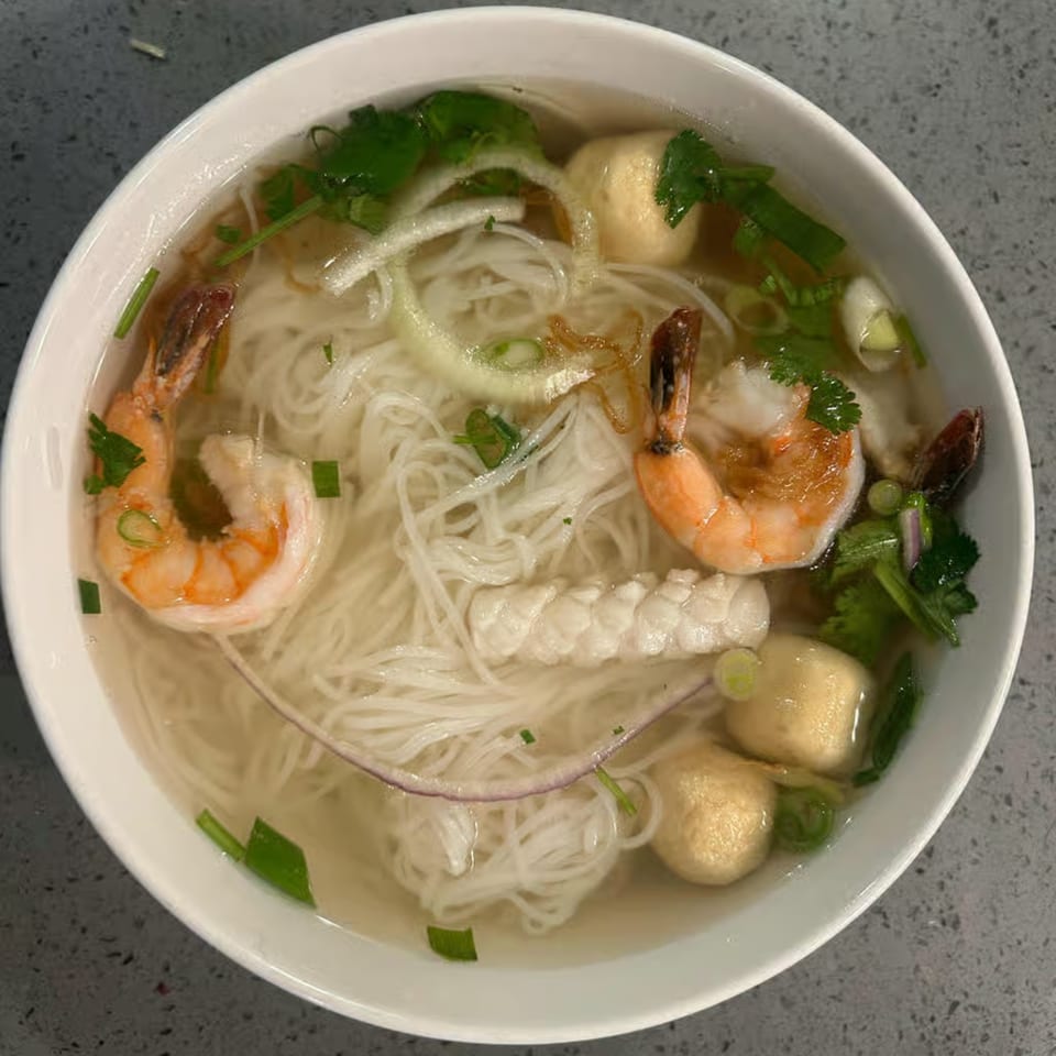 A bowl of Pho Teresa's Vietnamese pho with shrimp, noodles, fish balls, and herbs.